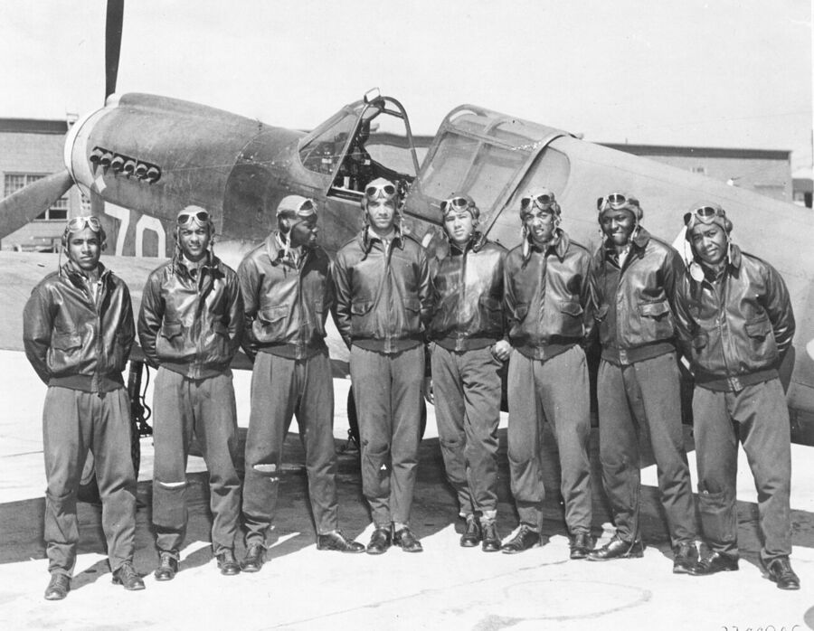 A cohort of the Tuskegee Airmen, standing in front of a plane.
