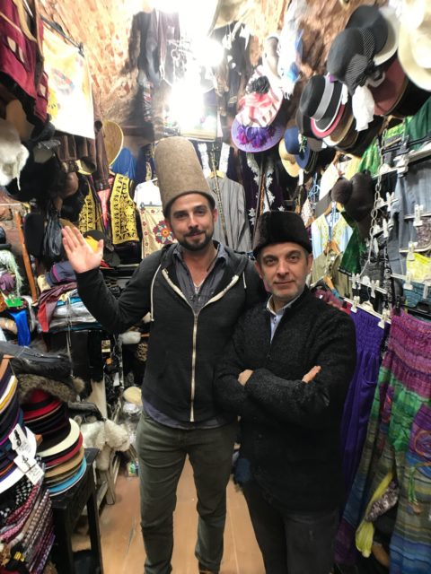 man wearing traditional turkish hat in a store surrounded by hats with the hat seller