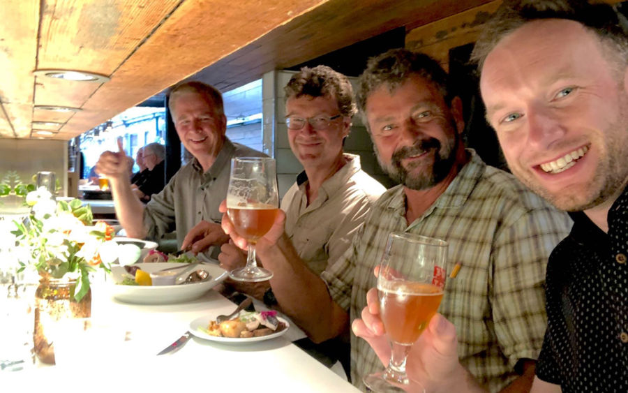colin mairs, simon griffith, karel bauer, and rick steves smiling at a restaurant bar and holding beverages